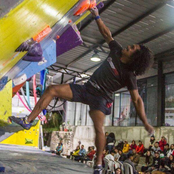 Escalador en un movimiento dinámico durante una competencia de boulder indoor.