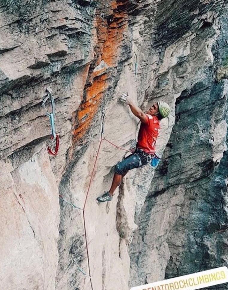 Escalador deportivo asciende una pared de roca junto a varias cintas exprés.