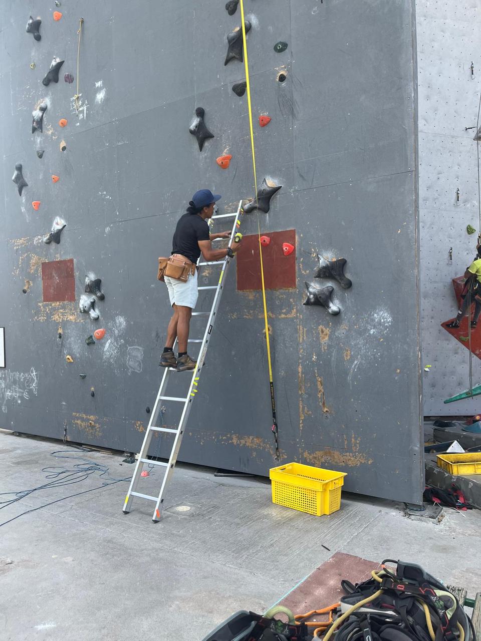 Armador trabaja en un muro de escalada desde una escalera.